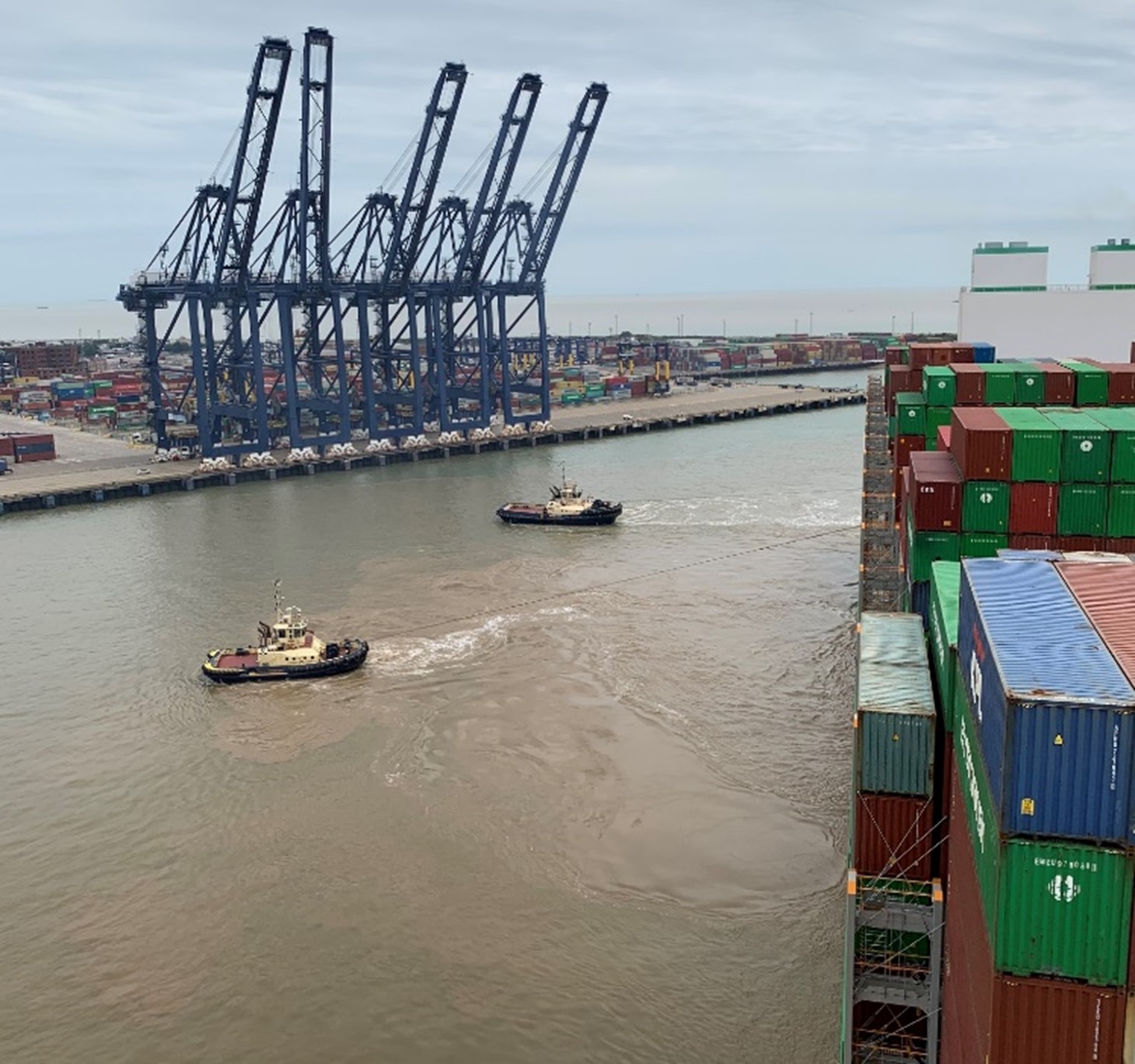 view of blue cranes in port being approached by a container ship