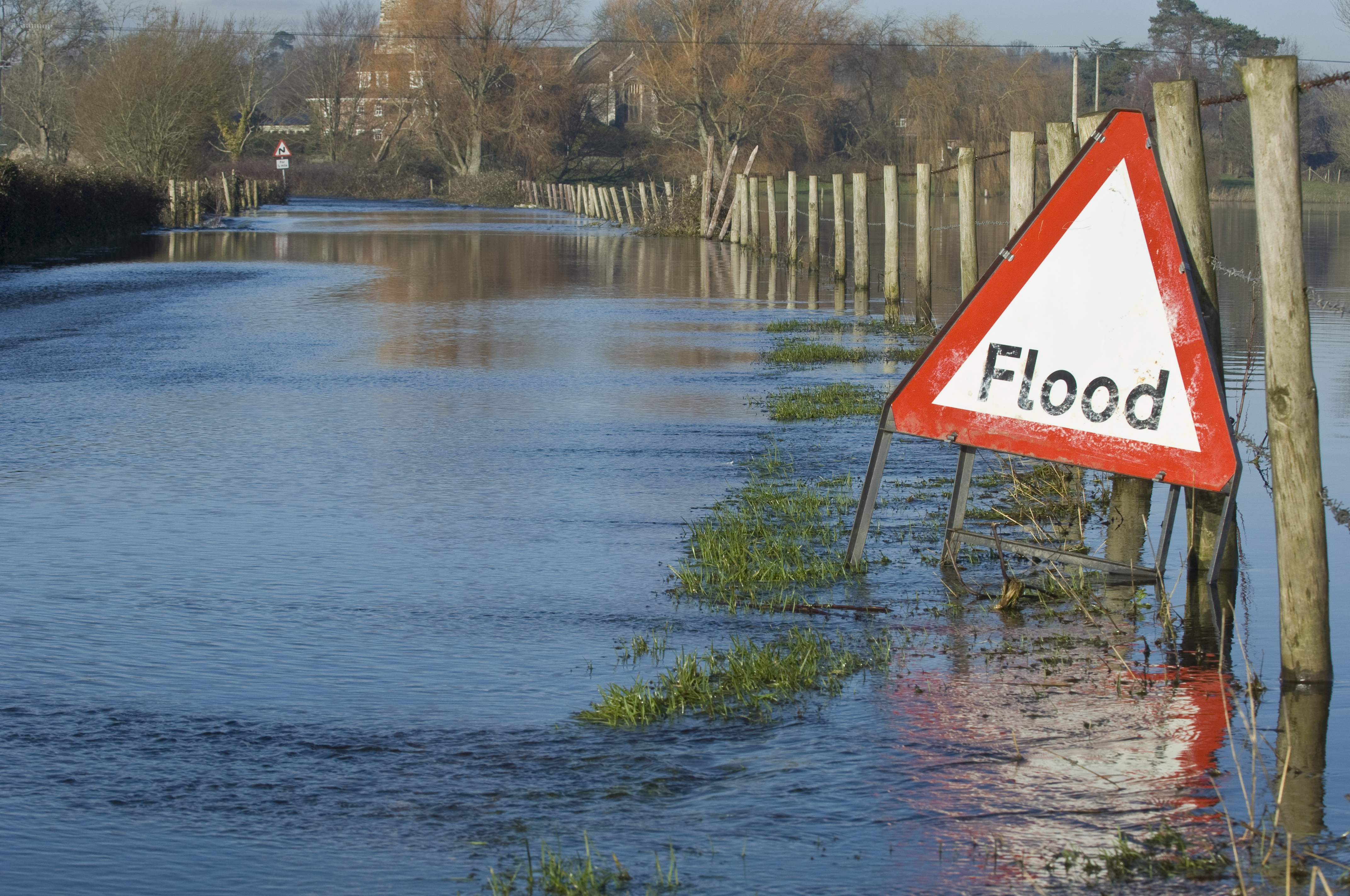 Image of a flooded road with a flood sign warning in the UK