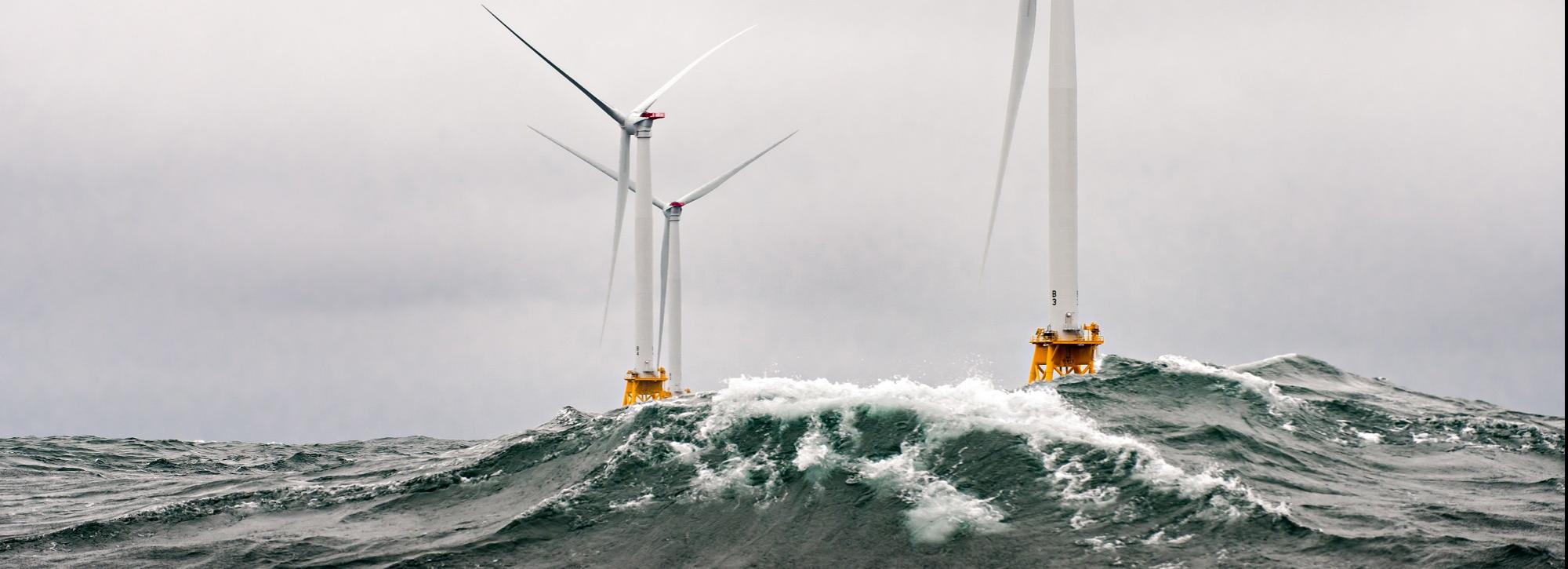View of two wind turbines in turbulent grey sea with waves