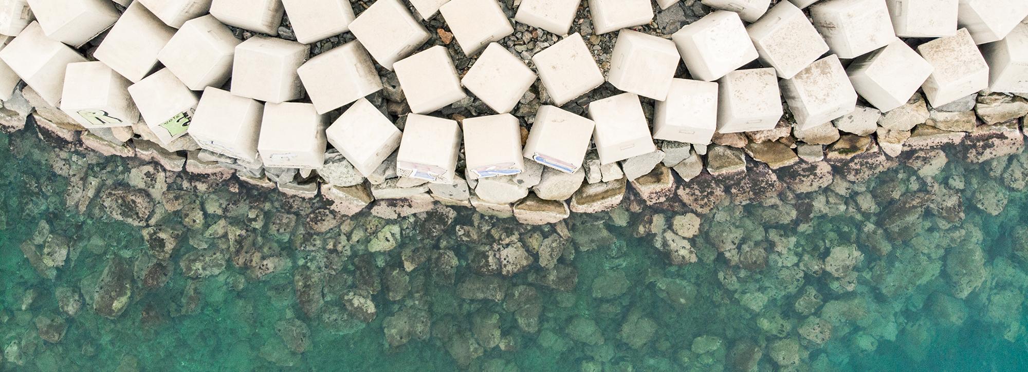 Aerial view of white armoured breakwater in green sea waves