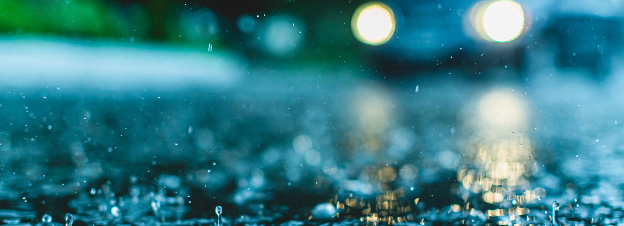 close up view of splashing rain on road with car lights
