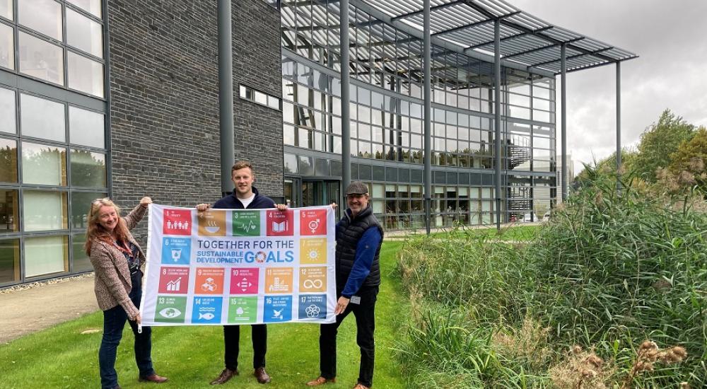 Three people holding SDG flag in front of office building in Howbery Park, Oxfordshire
