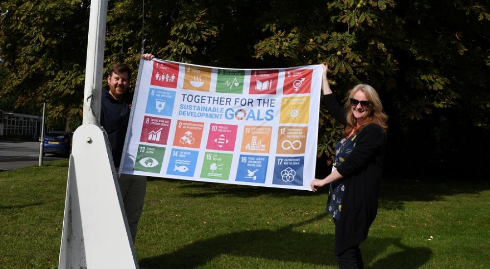 Two people holding SDG flag on green grass
