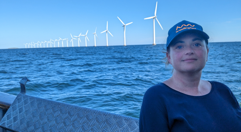 Female scientist, Kerry Marten, on a boat in the Danish Sea, in front of sea wind turbines