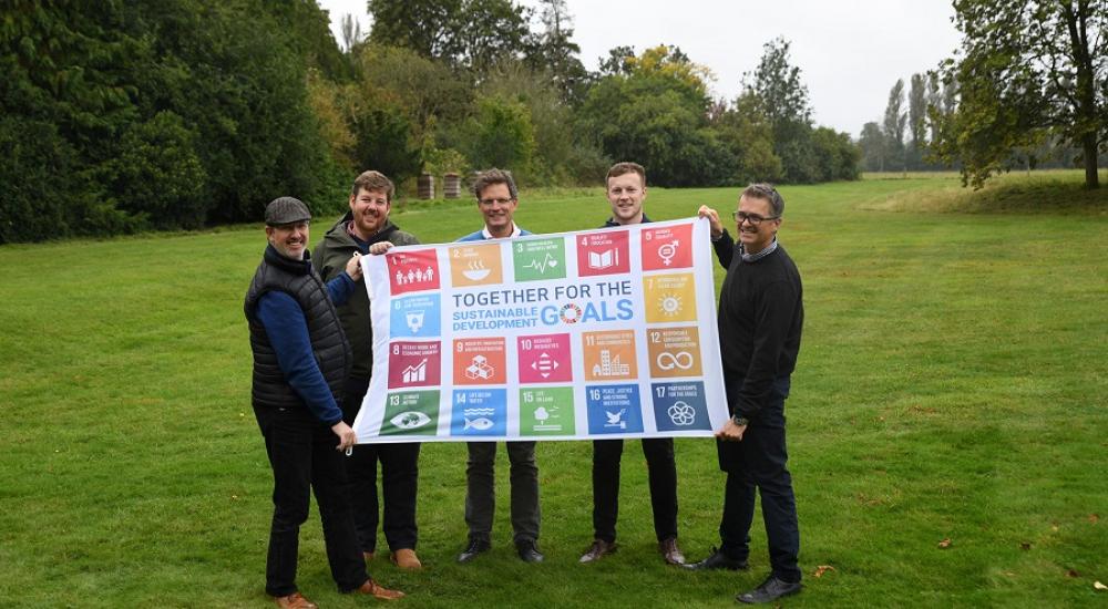 4 people from HR Wallingford holding one big SGD flag on green grass