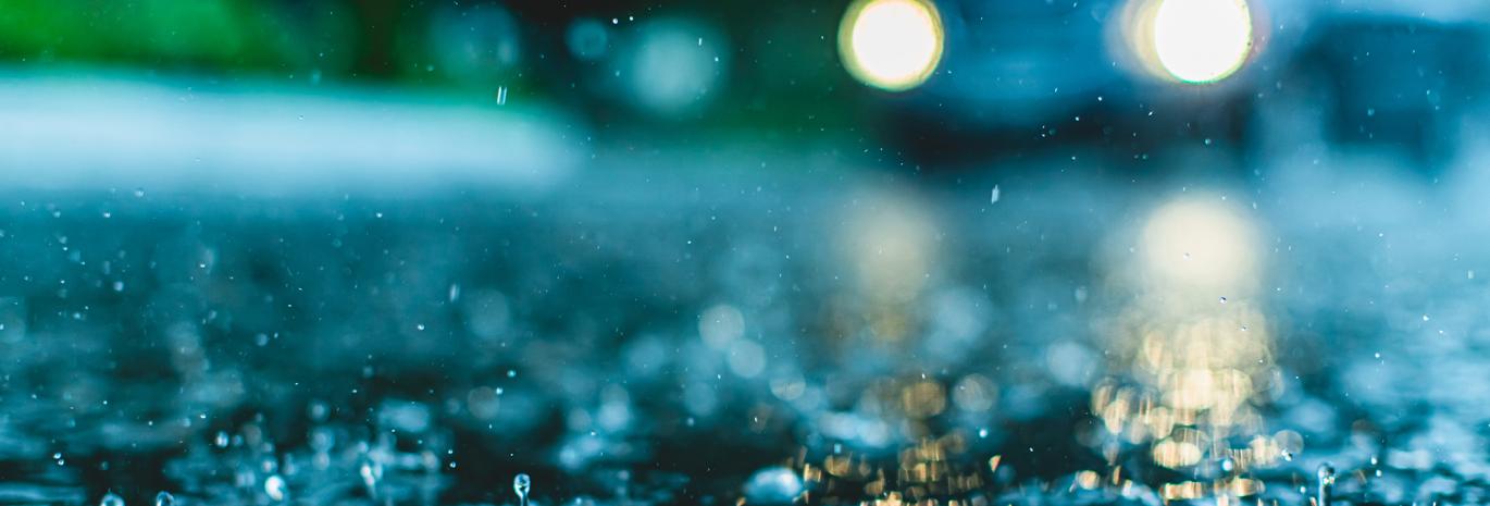close up view of splashing rain on road with car lights 